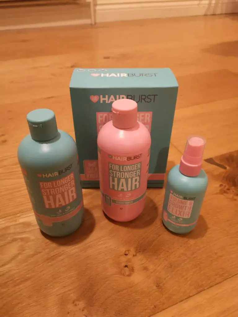 Bottles of Hairburst Shampoo, Conditioner and Elixir, standing in front of their cardboard box, on a wooden floor.