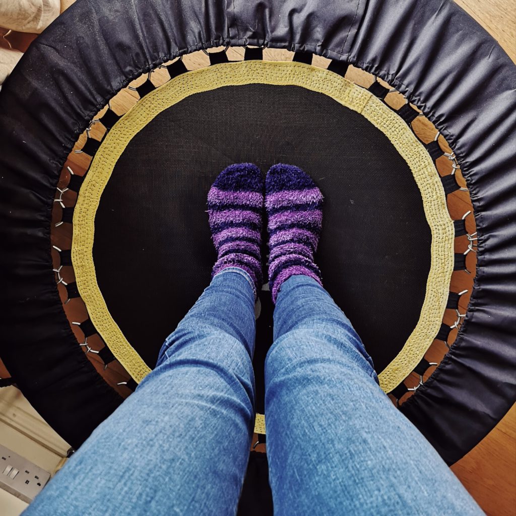 A pair of legs wearing blue jeans and stripy purple socks, standing on a trampette