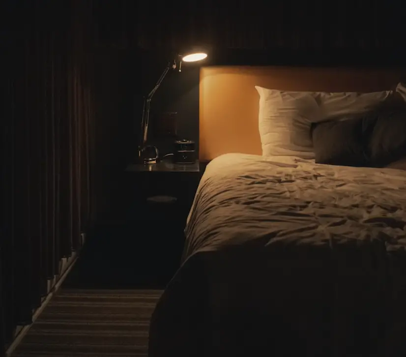 A bed with a bedside lamp alongside it, switched on.