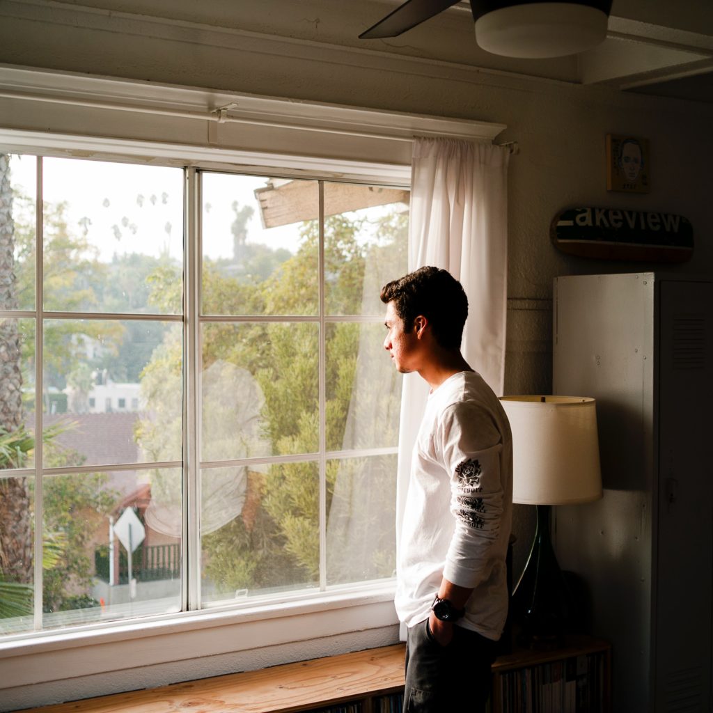 A man indoors looking out a window.