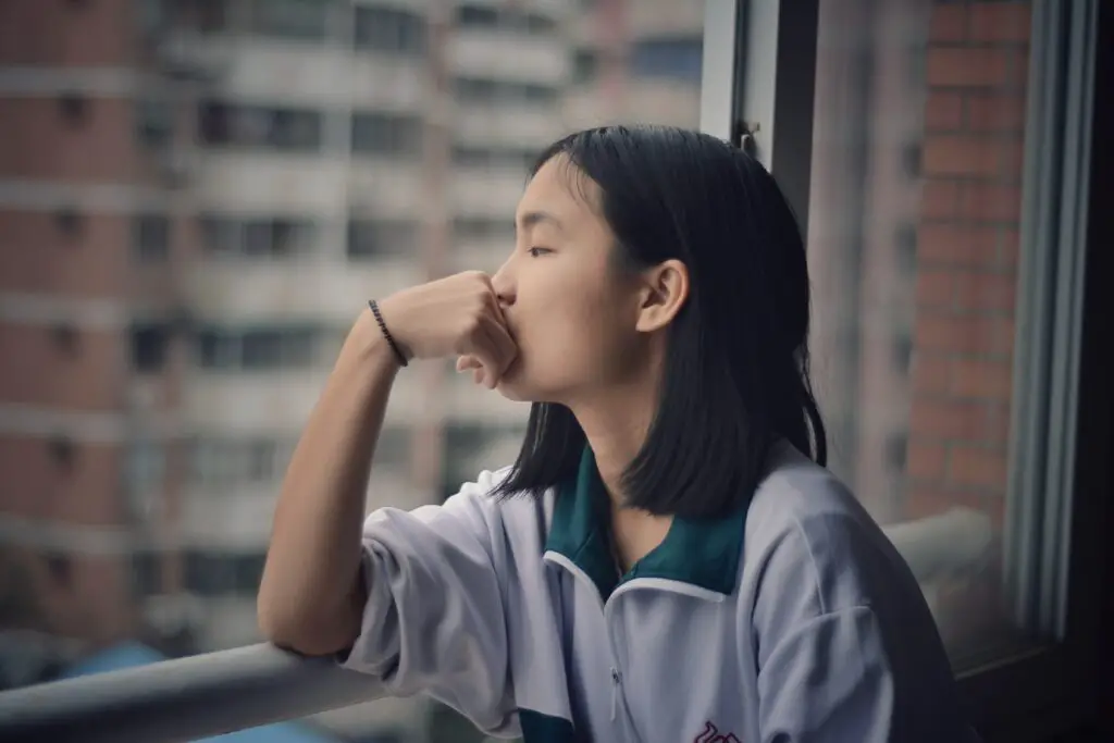 A woman staring out of a window with her hand on her chin, deep in thought