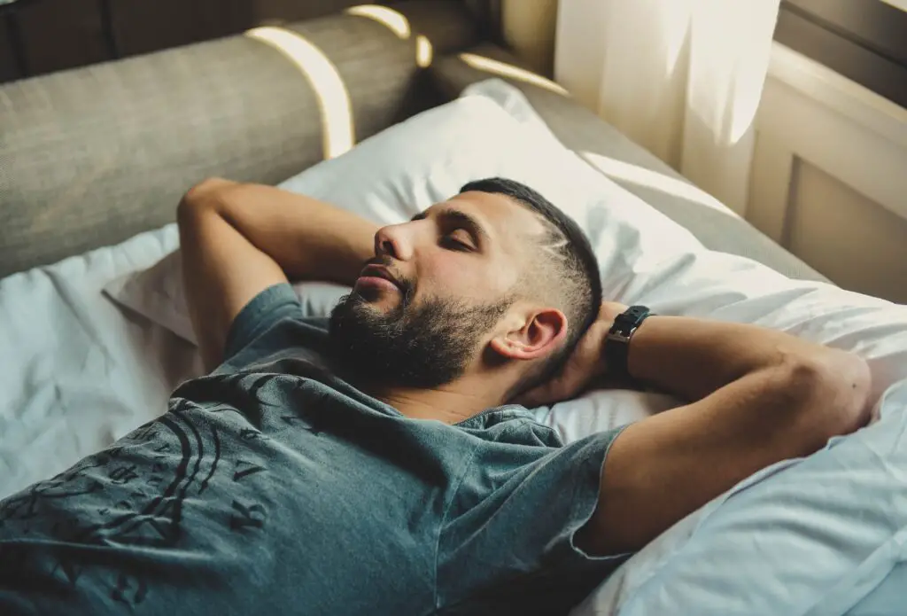 A man laying asleep on his back with his hands behind his head