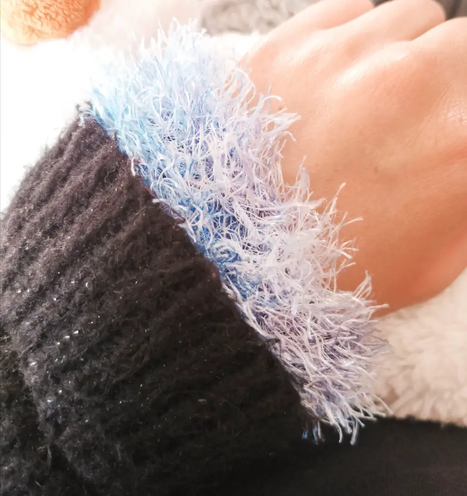 Light blue knitted wrist warmer on my wrist, tucked into the sleeve of my black jumper.