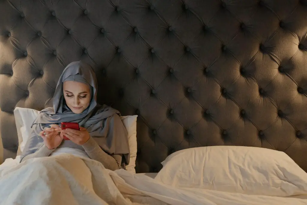 A woman scrolling on her phone whilst sitting up in bed.