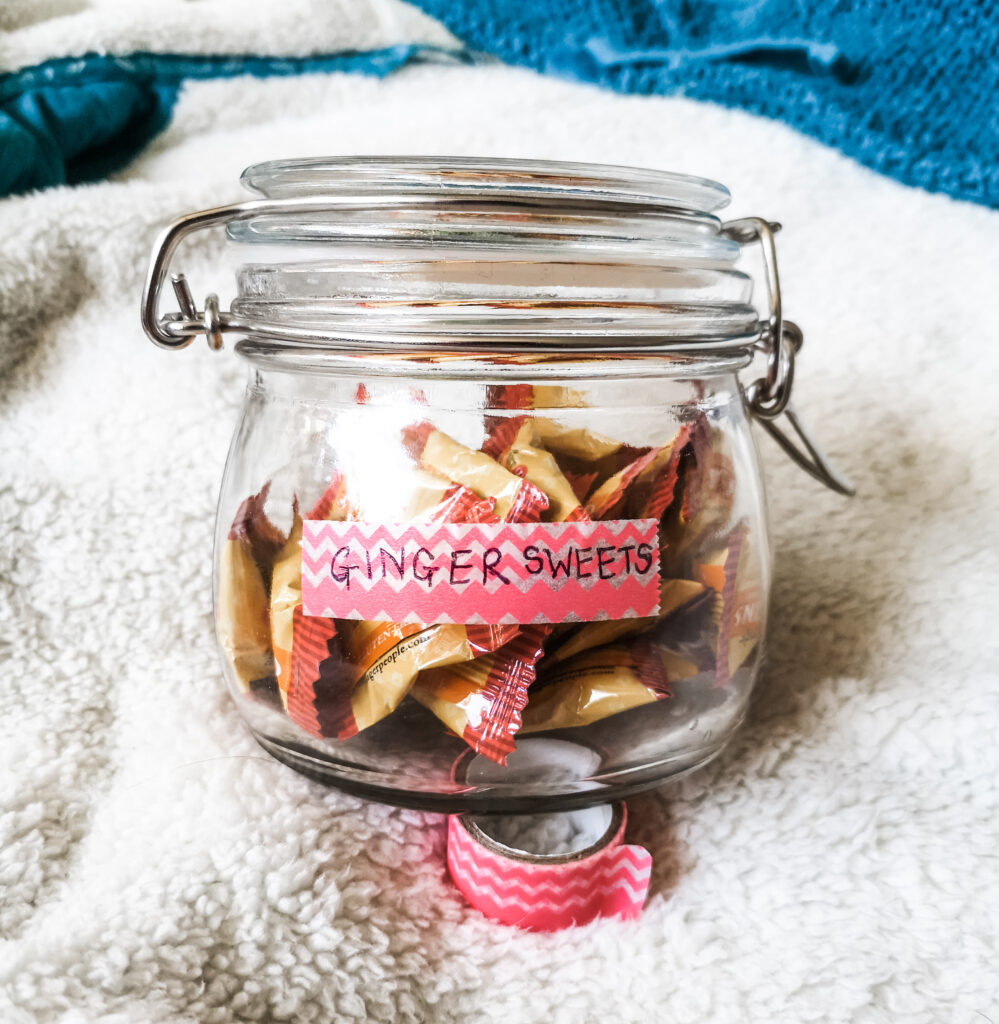 A glass jar of ginger sweets that has been labeled 'ginger sweets' using a strip of pink, zig-zag pattered washi tape.