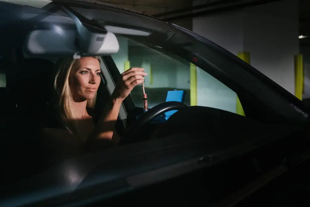 A woman applying lip gloss in a car.