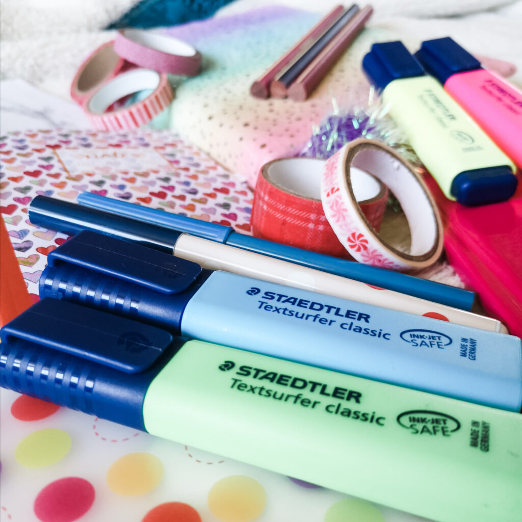 A selection of colourful stationery including notebooks, highlighter pens, washi tape, colouring pencils and pens.