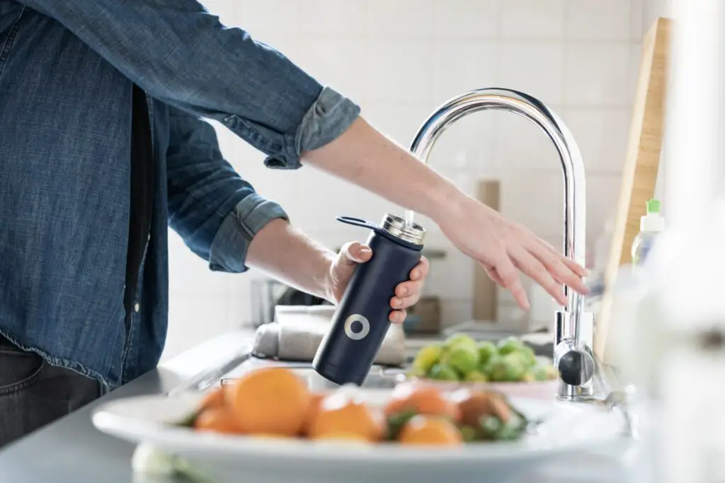 A person filling up a black water bottle from a kitchen tap.