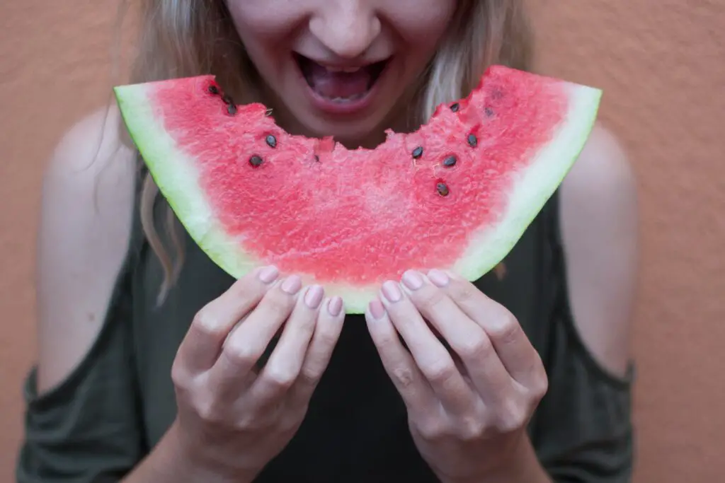 A woman holding a slice of watermelon which she has taken a bite out of.