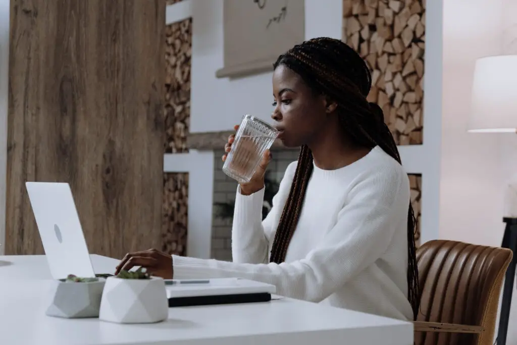 A woman working on her laptop and drinking a glass of water.