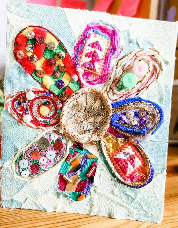 A handmade greetings card featuring a flower made up of scraps of material, thread, sequins and beads.