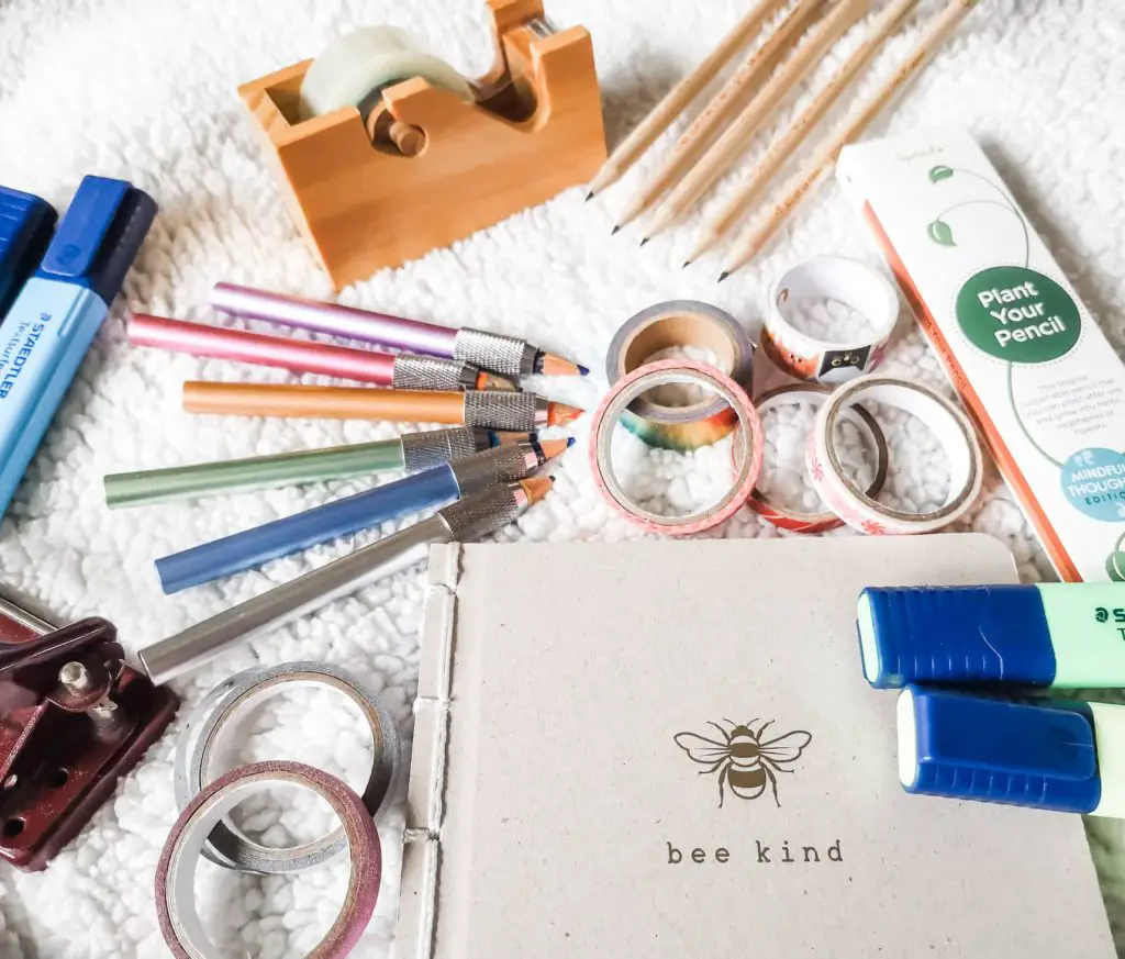 A flatlay of stationery including pencil extenders, washi tape, highlighters, pencils and a wooden tape dispenser.