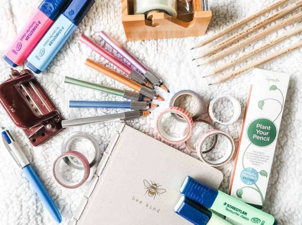 A flatlay of sustainable stationery including washi tape, pencil extenders, highlighters and a notebook.