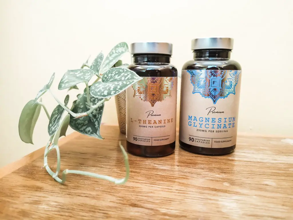 Two bottles of supplements (L-Theanine and Magnesium Glycinate) on a wooden surface with a plant next to them