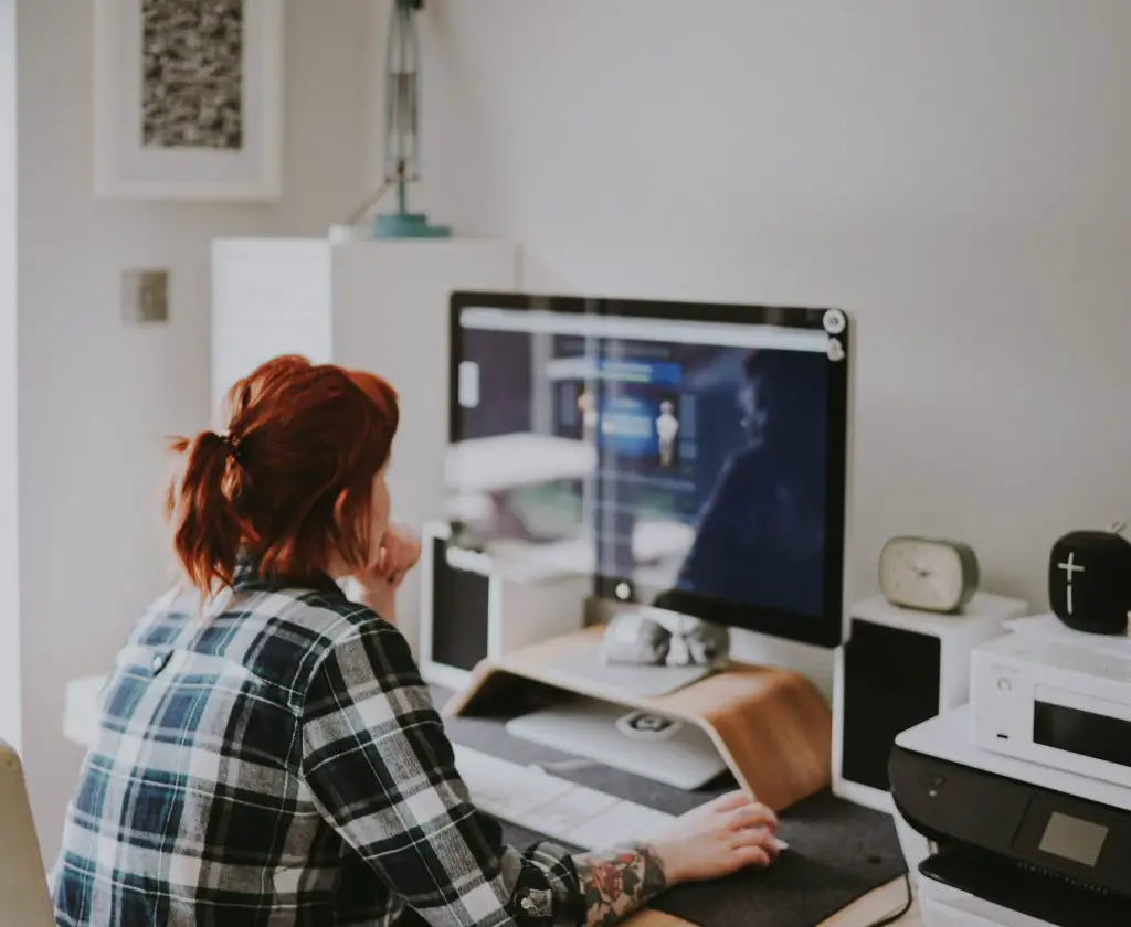 A woman with red hair, wearing a checked shirt and working on a computer.