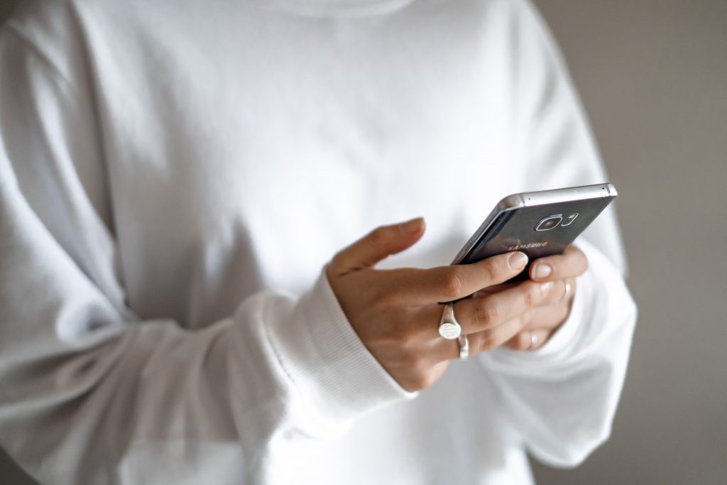 A woman wearing a white sweatshirt and typing on a mobile phone.