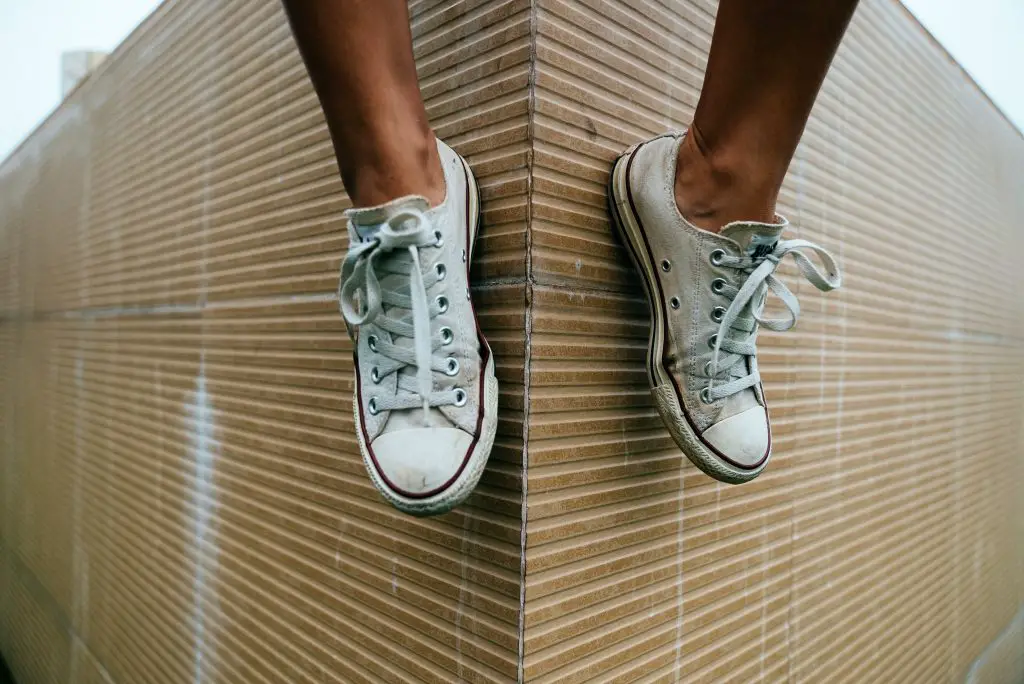 A pair of off-white converse-style shoes worn by somebody sitting on a wall with their legs hanging down.
