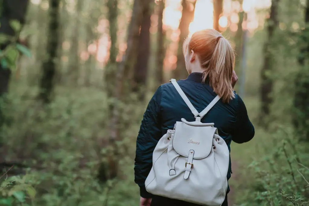 A woman walking in nature. She is wearing a dark blue jacket and a white rucksack.