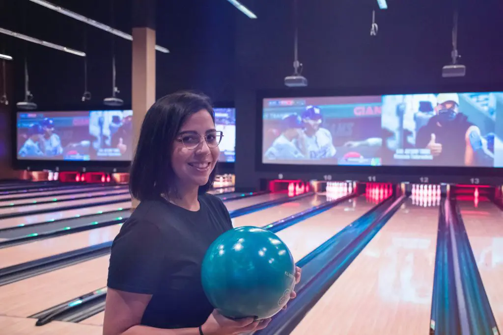 A woman holding a bowling ball and smiling in a bowling alley.