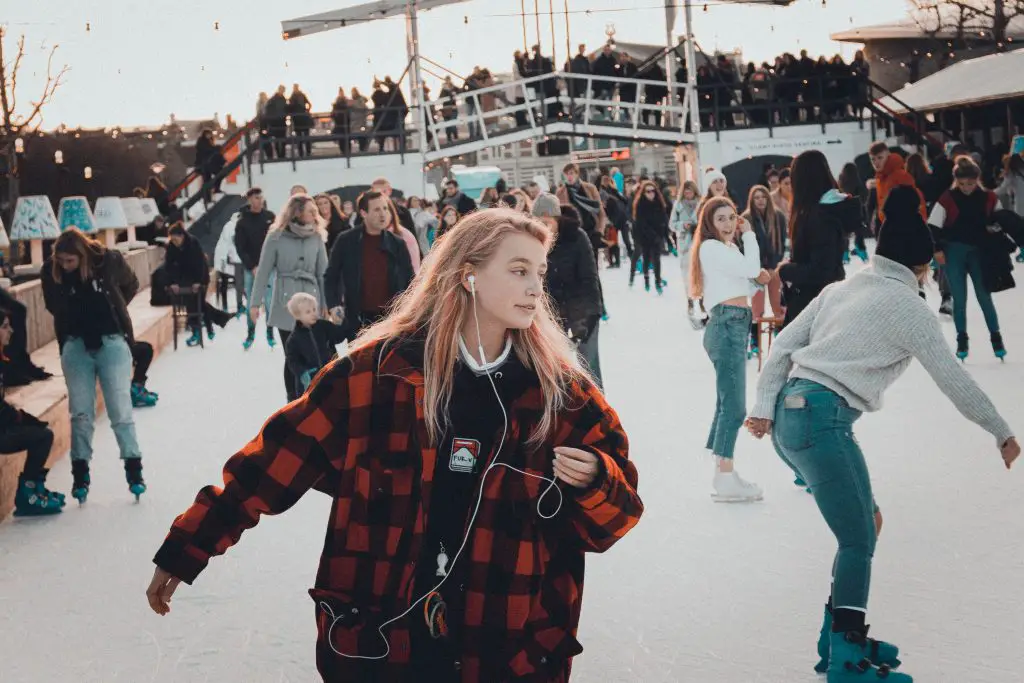 A woman ice-skating on an outdoor ice rink. There are lots of other skaters in the background.
