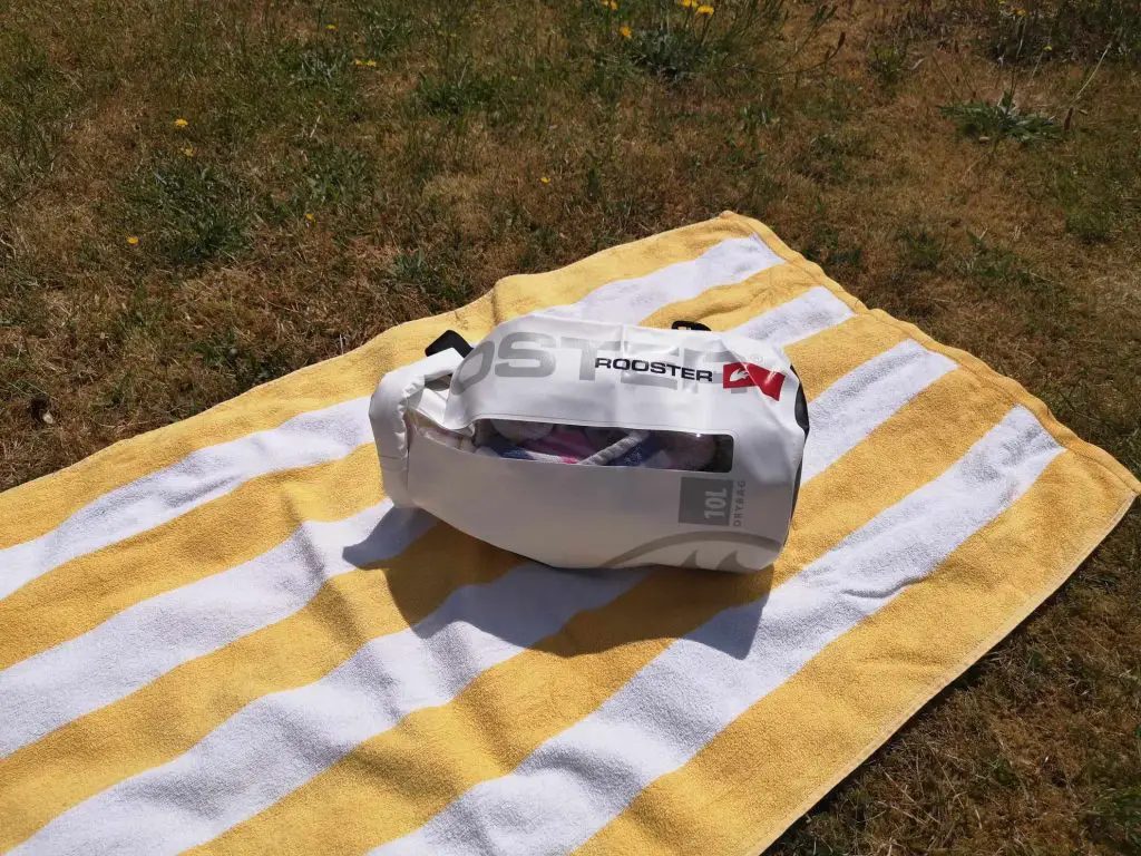 A filled white dry bag by Rooster, laying down on a yellow and white striped towel.