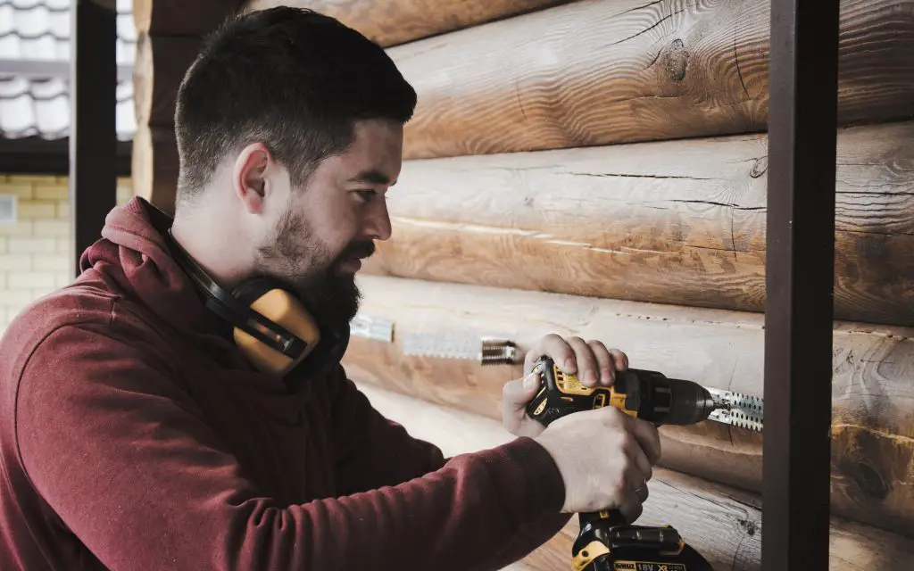 A man using a drill and other equipment to make holes in a log wall.