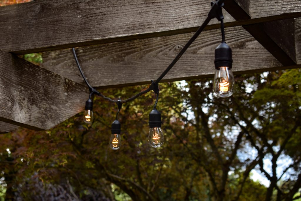A string of outdoor lights hanging on a wooden arbor.