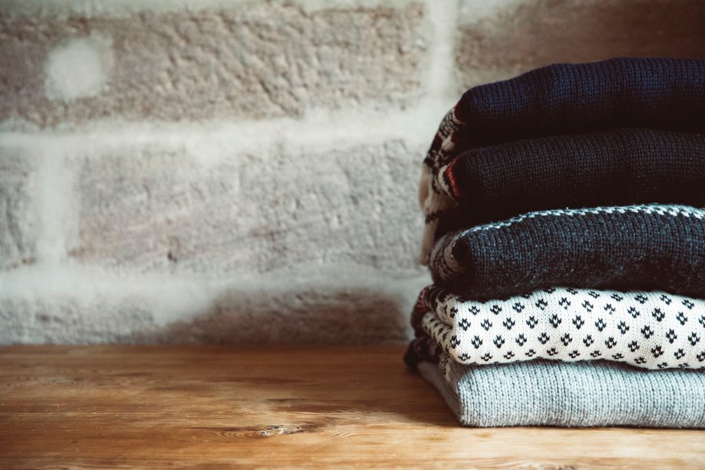 A pile of knitwear jumpers on a wooden surface.