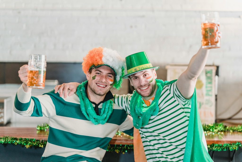 Two men dressed in green attire, celebrating St Patrick's Day with drinks in their hands.