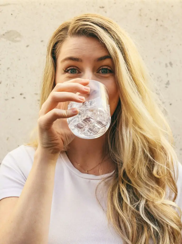 A woman drinking a glass of water with ice in it.