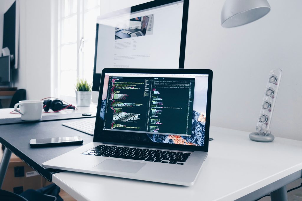 An open laptop on a desk, with coding programmes on the screen.