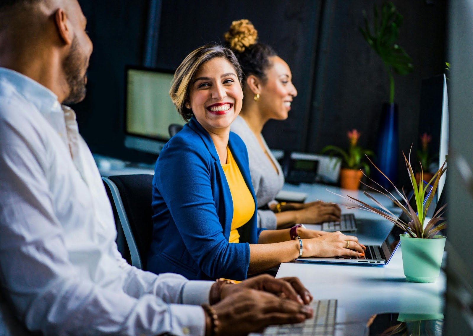 Three people working at laptops and smiling at each other.