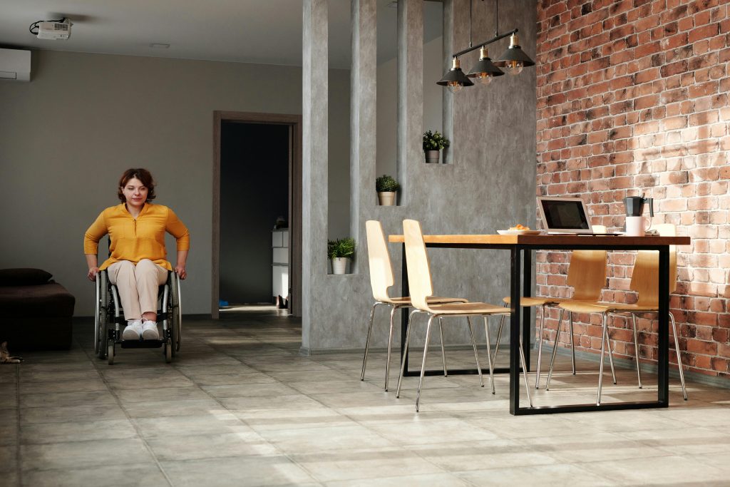 A woman in a wheelchair wheeling herself across a tiled floor in a house.