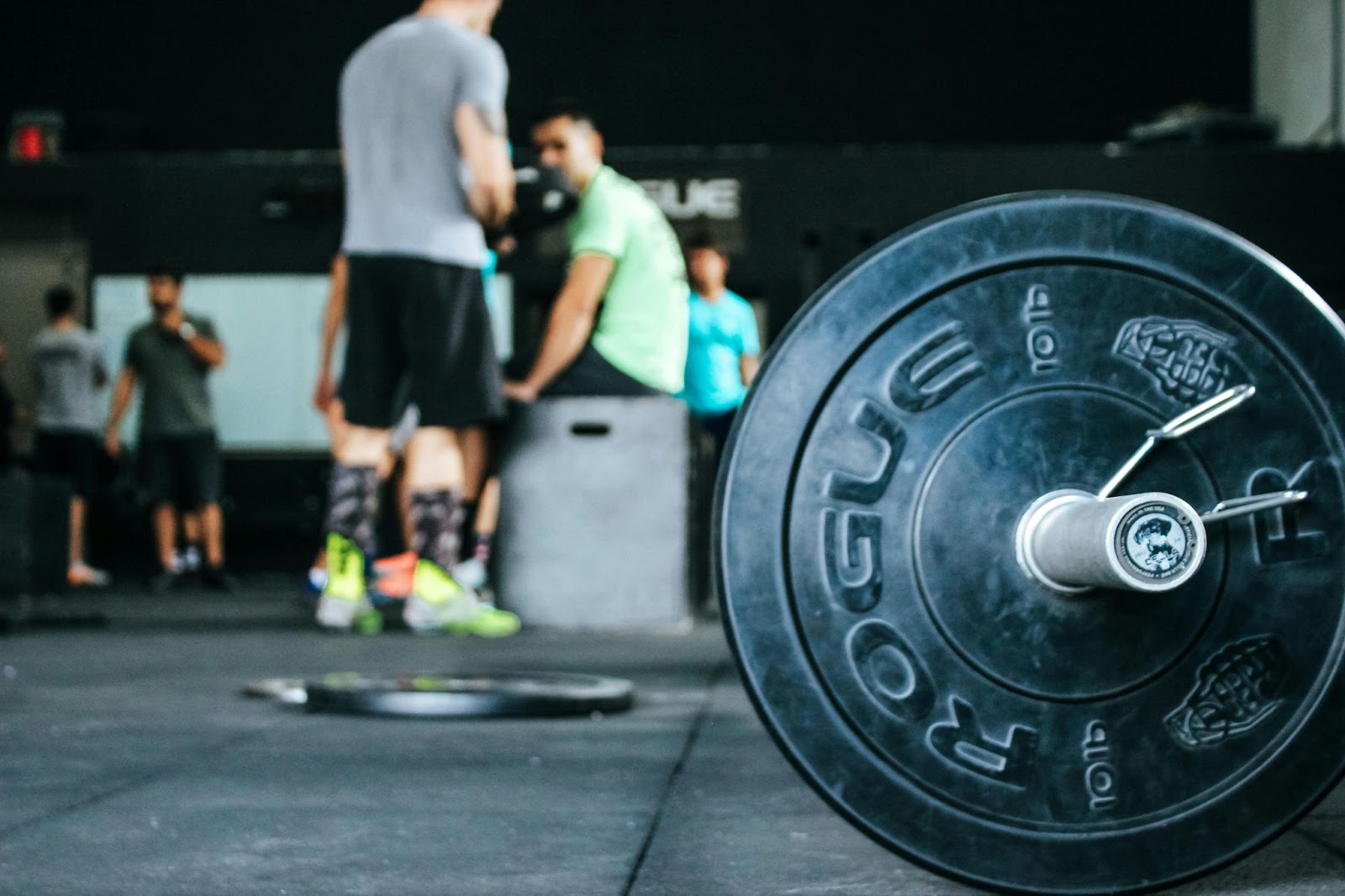 A gym environment featuring barbells and athletic people standing and sitting.