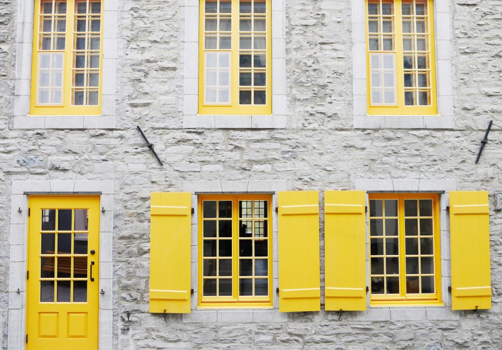 The exterior of a grey stone house with yellow door and window frames and shutters.