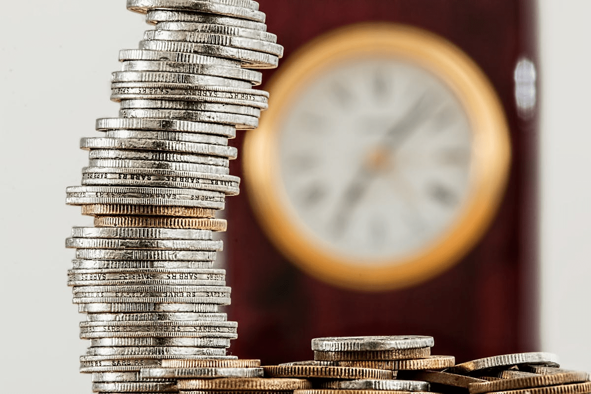 A pile of silver and gold coins with a clock in the background.