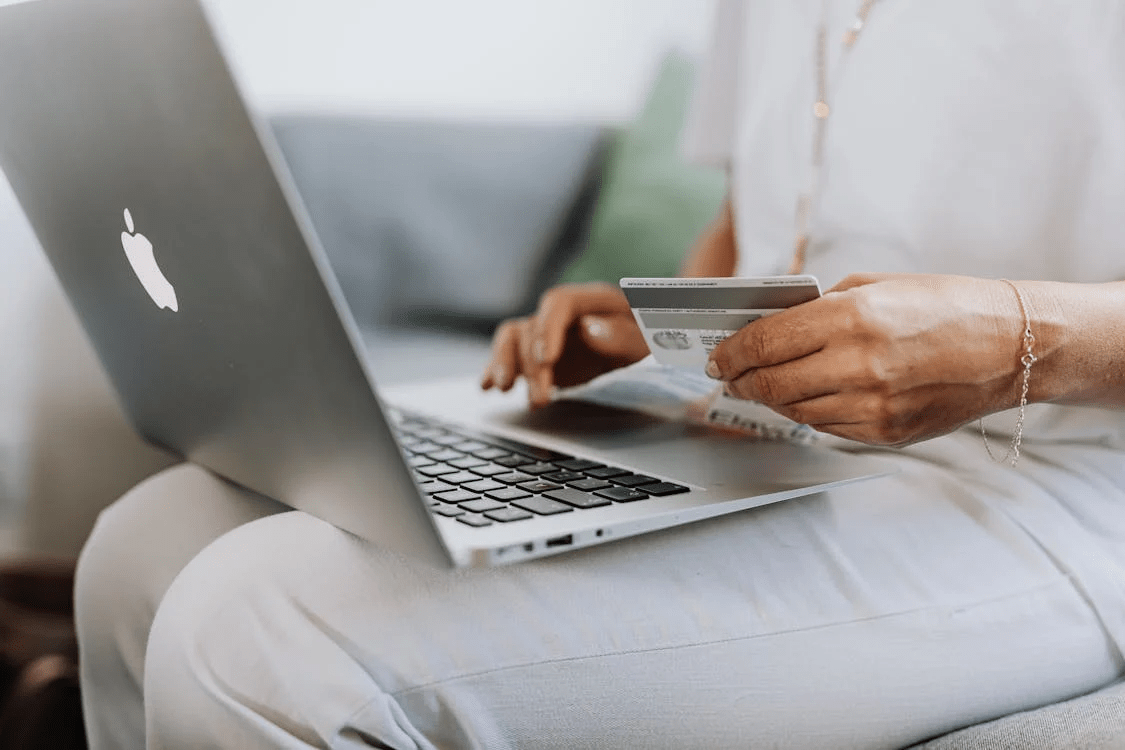 A person with a laptop on their lap, holding a credit card, possibly about to make an online purchase.