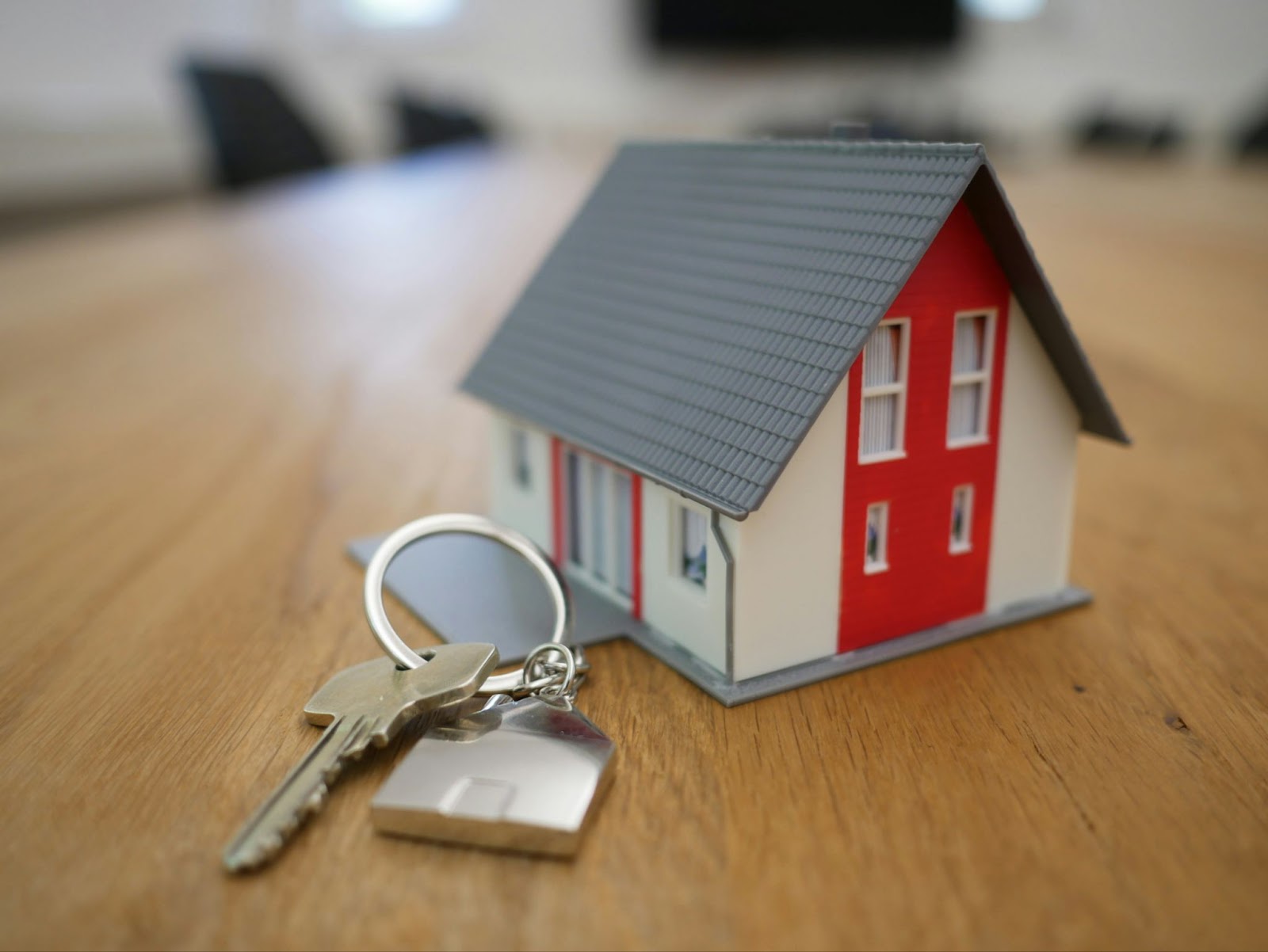 A model of a house, next to a house key on a keyring.