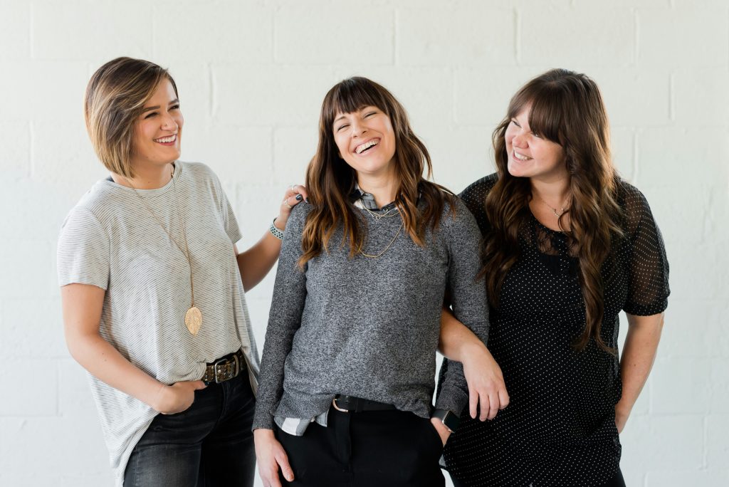 A group of three women, linking arms and smiling and laughing together.