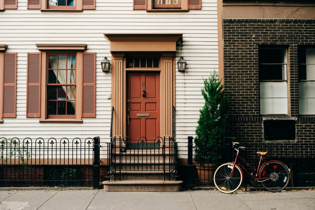 A picturesque terraced house with white painted cladding and pink shutters on the windows.