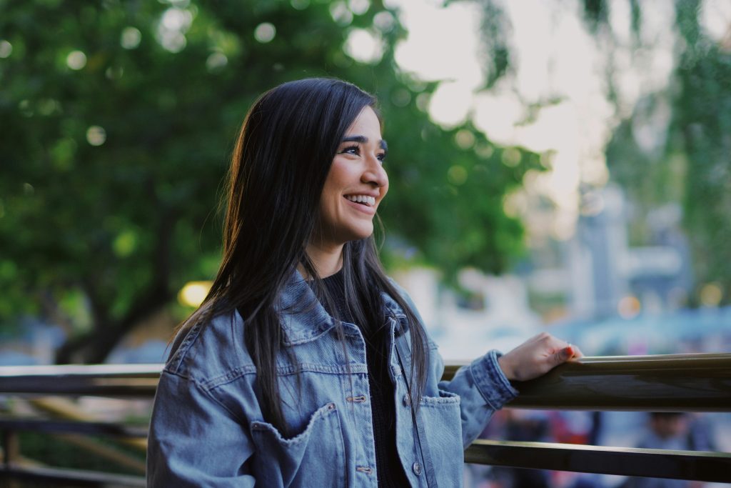A woman, standing outdoors, looking confident and smiling.