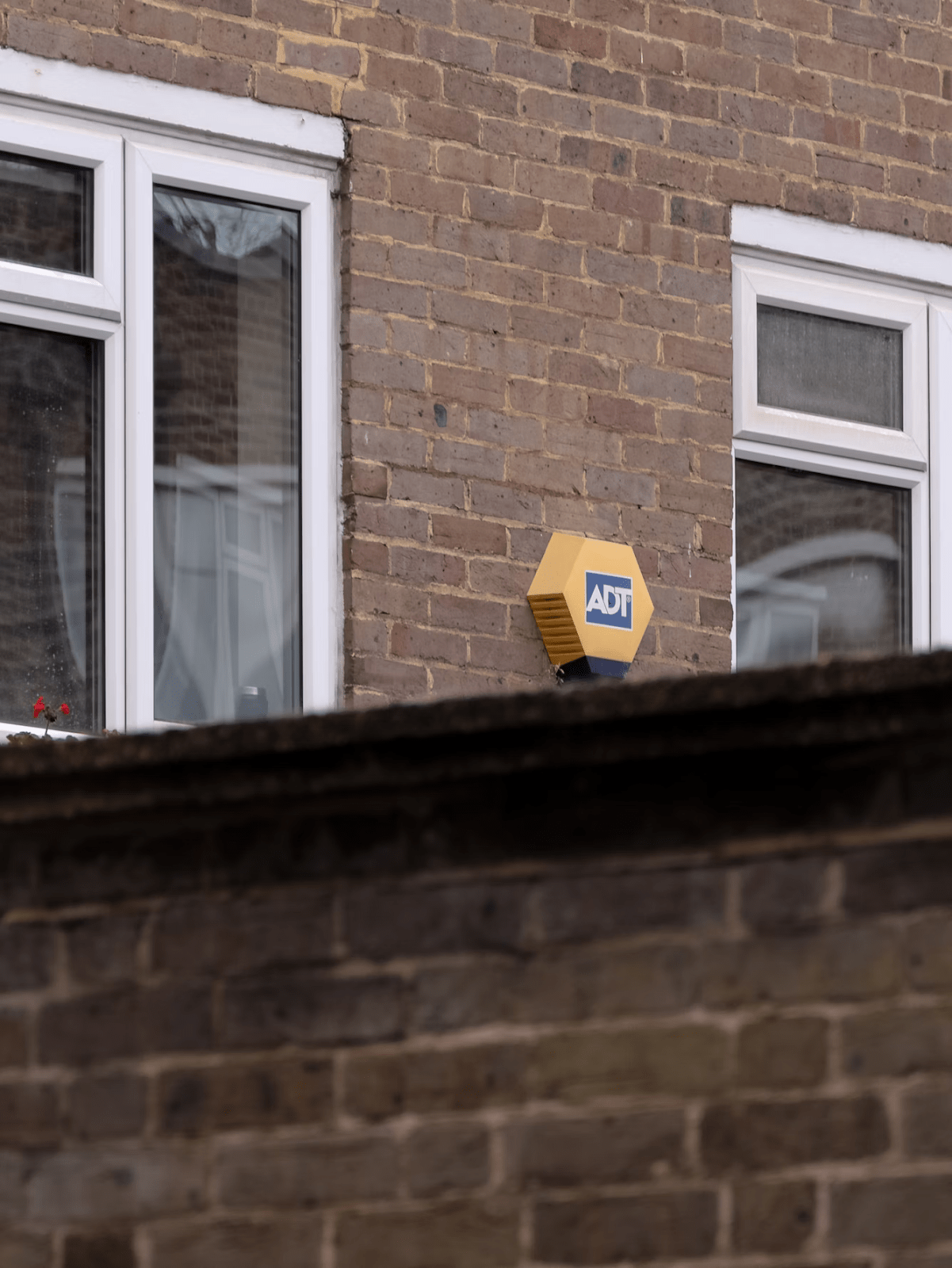 The wall of a house, with two windows and a burglar alarm.