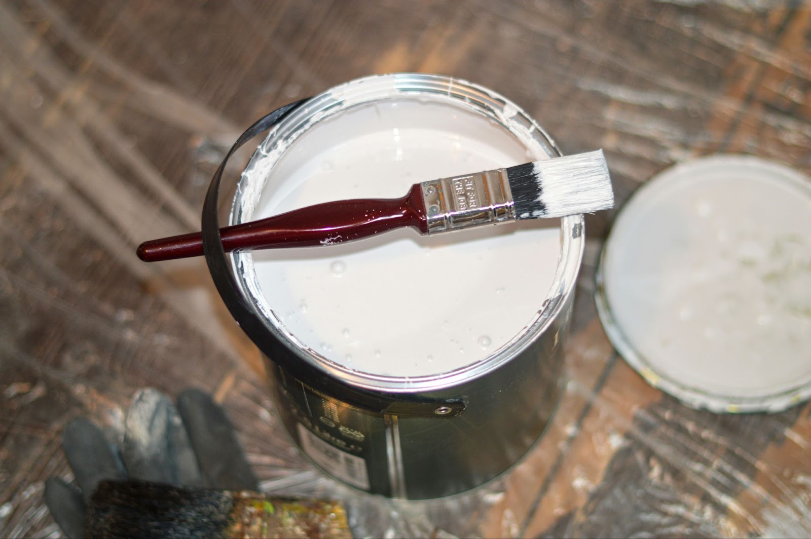An open tub of white paint with a paintbrush laying across it.