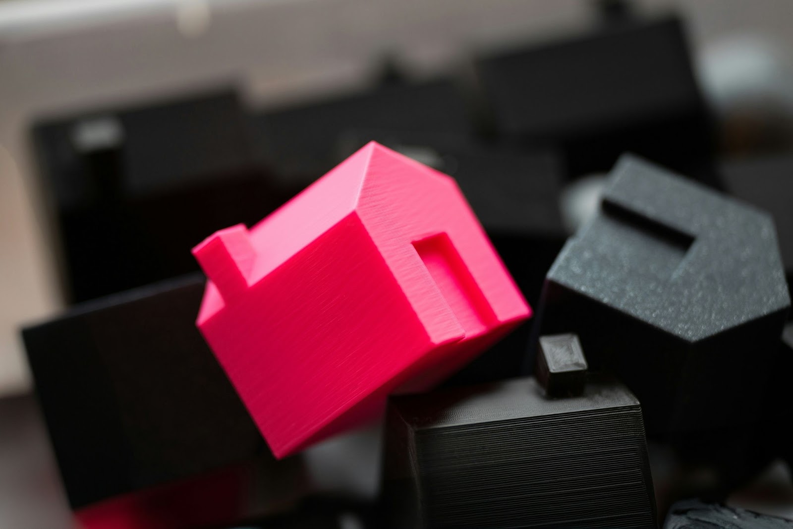 A pile of miniature models of houses, like those found in Monopoly. The one in the centre is bright pink whereas the others are black.